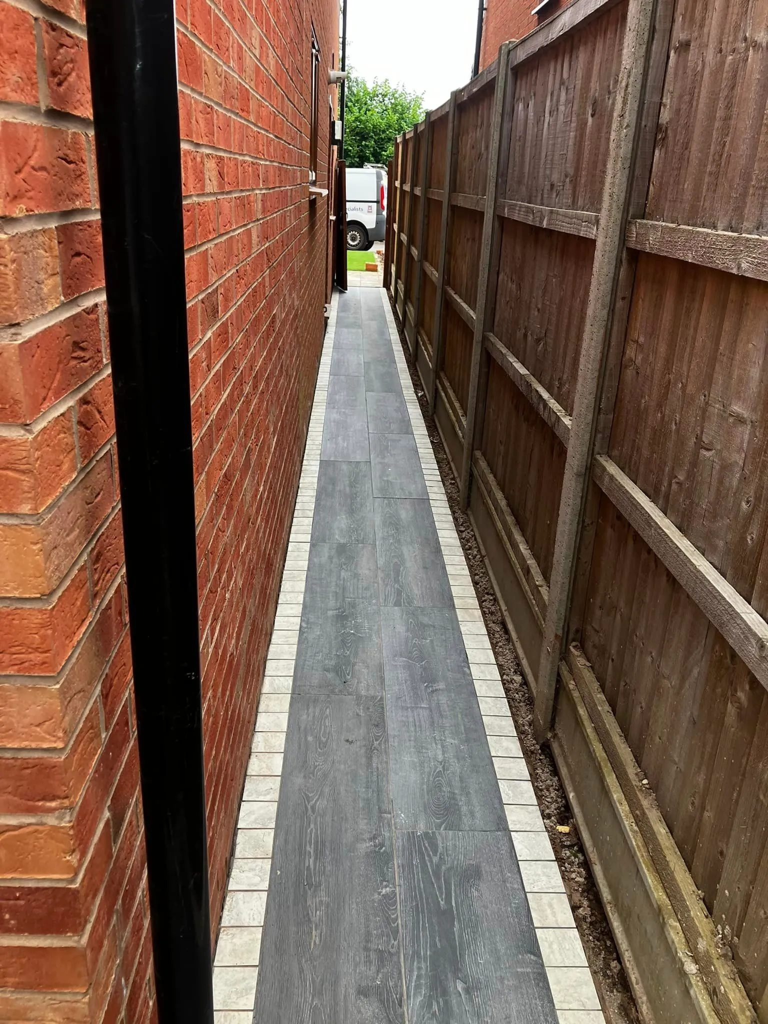 An alley way with a brick wall and a wooden fence.